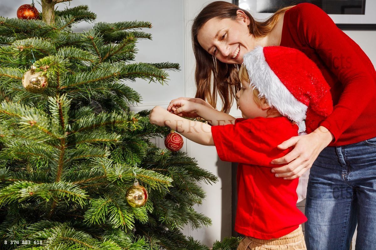 Mother and child decorating fresh Christmas tree with ornaments