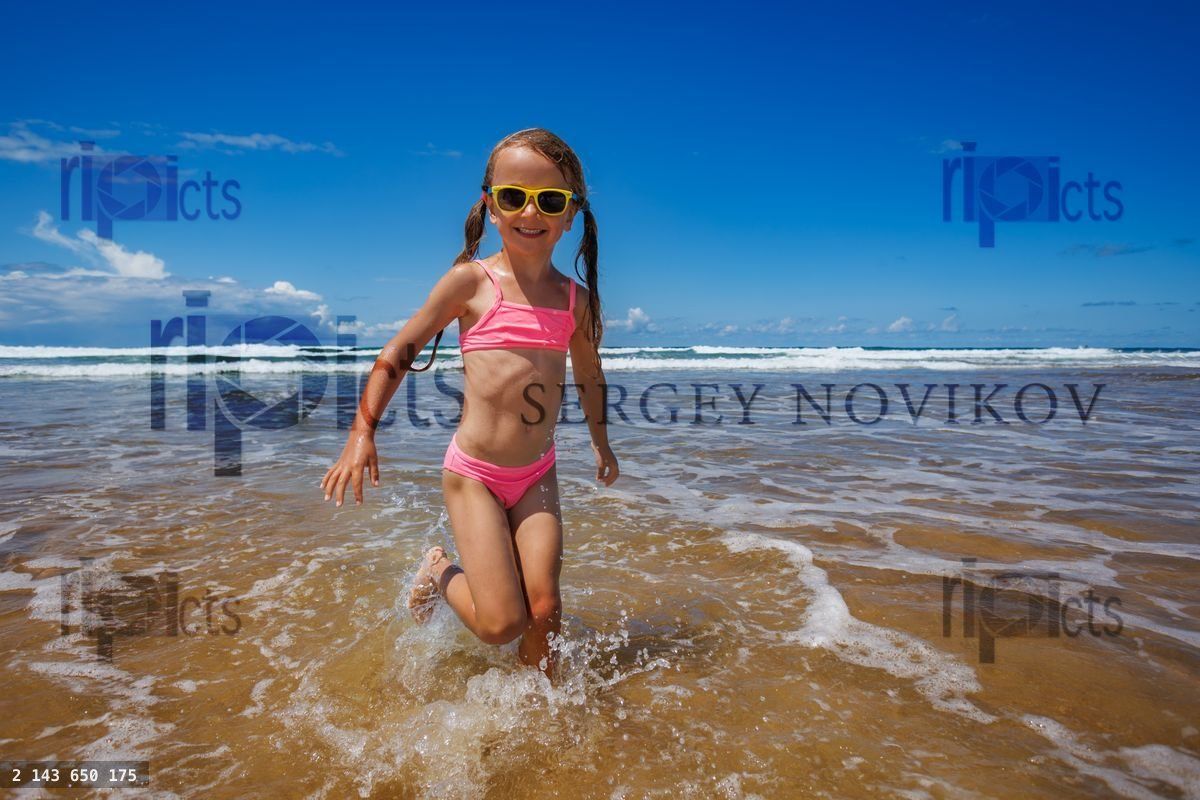 Young girl joyfully playing splashing in ocean waves on beach