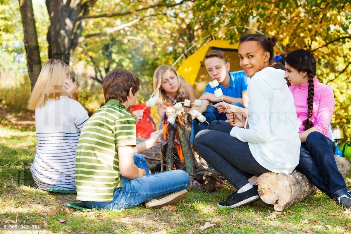 Friends hold marshmallow and sitting near bonfire