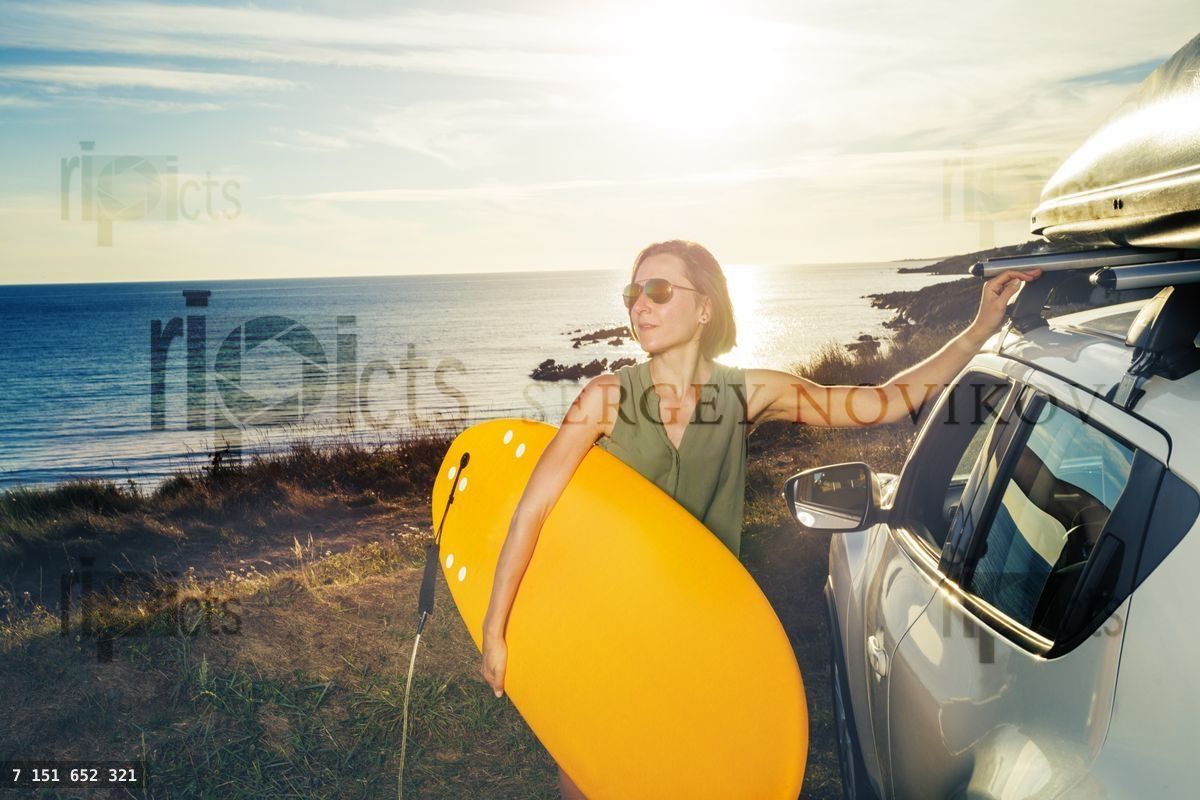 Woman on the cliff stand with surfboard over ocean sunset