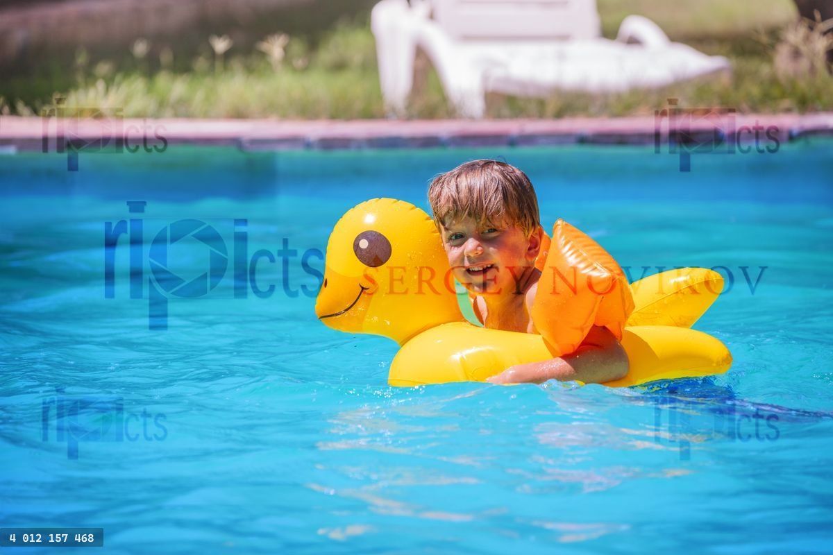 Young blond swimmer boy use a duck ring swim in summer pool