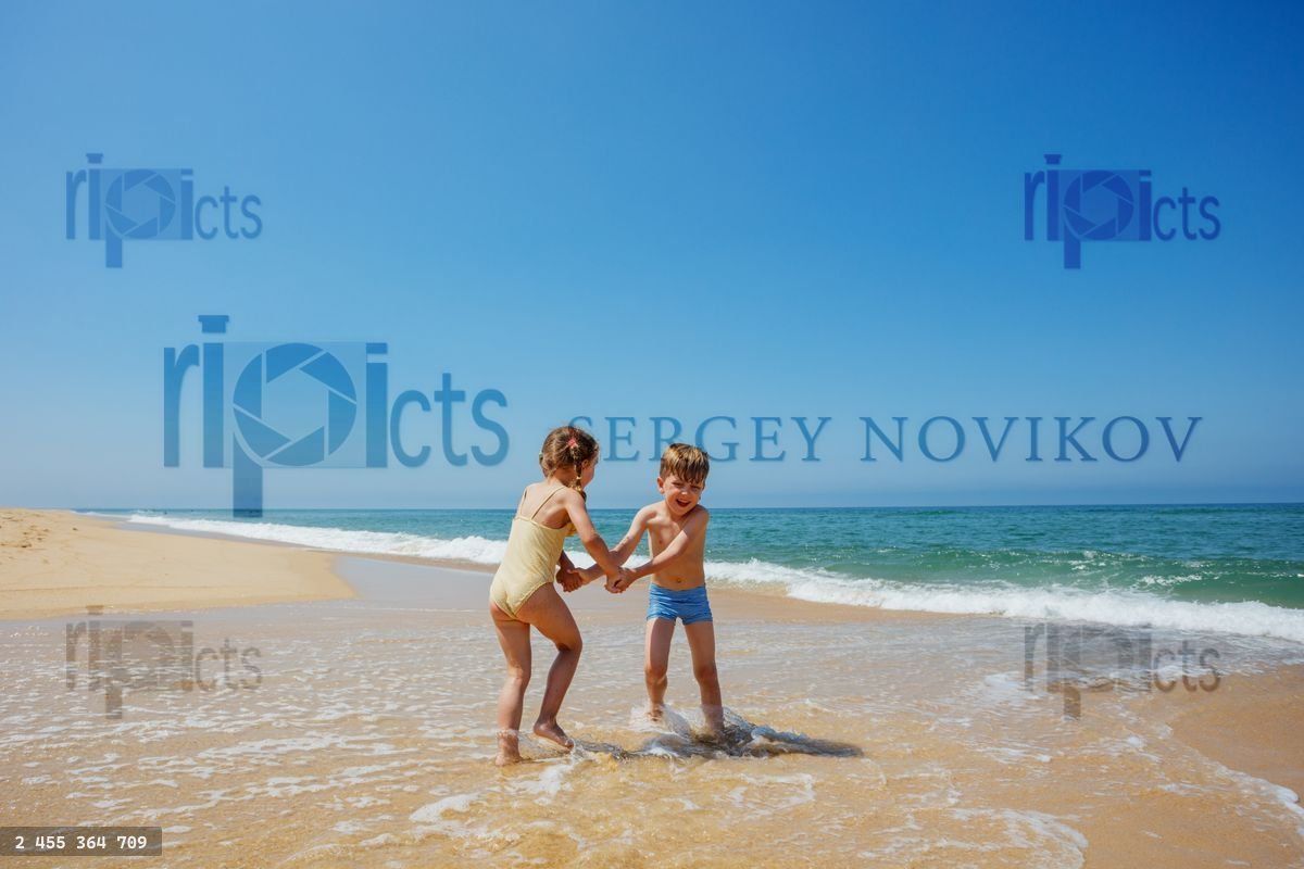 Young friends laughing and running on the sandy beach in waves