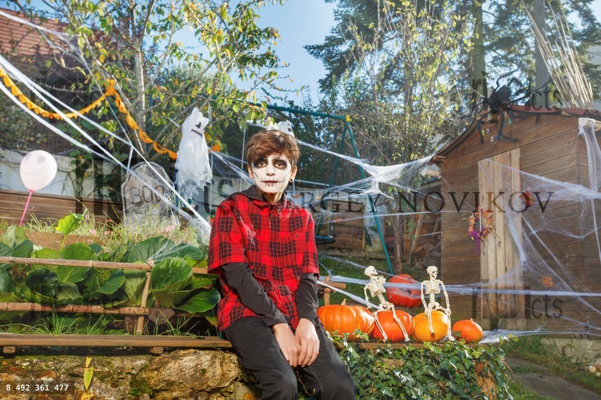 Young skull faced child poses beside Halloween props in yard