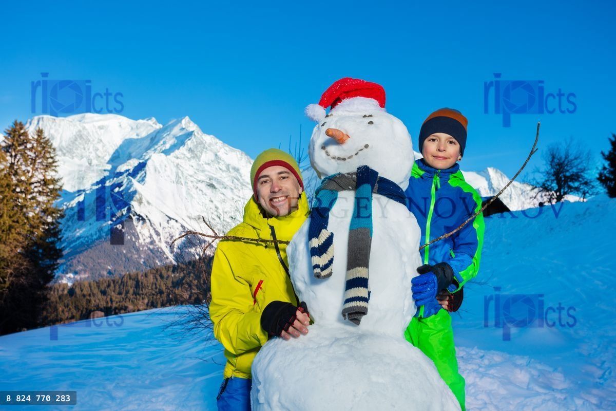 Plaisir en famille, un père et un garçon construisent un bonhomme de neige avec une écharpe et une carotte
