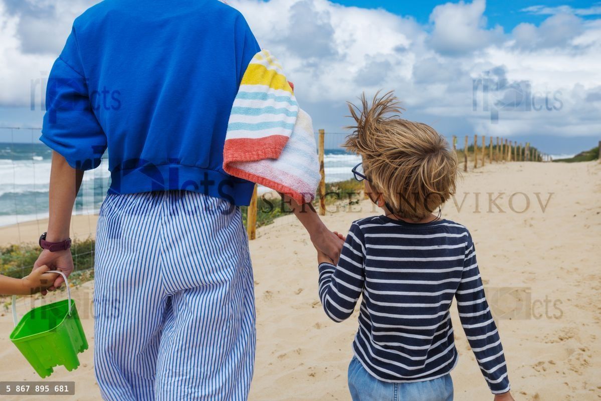 Woman with kid walking along beach path hold towel and bucket