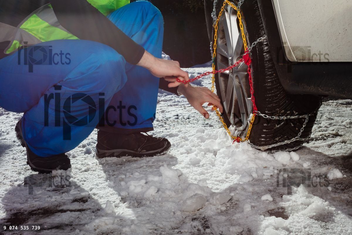 Close up of the man putting winter chains on car wheel