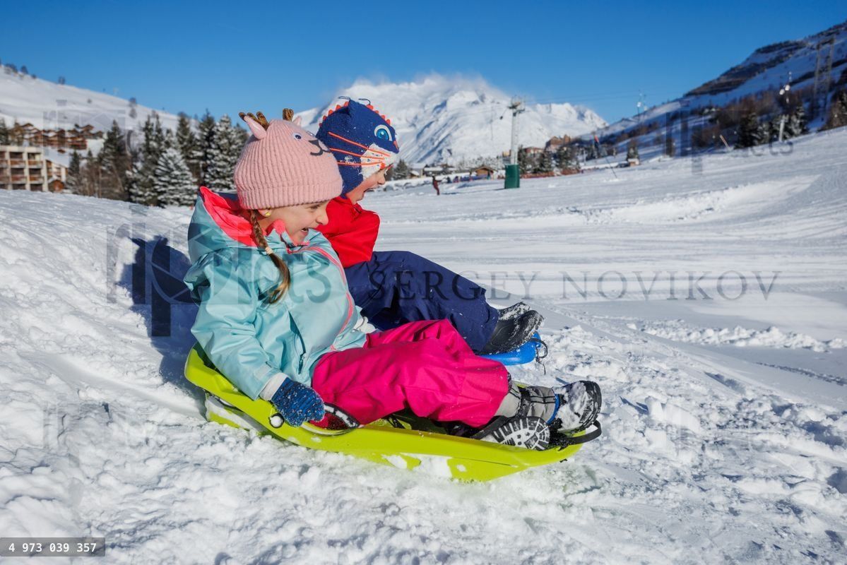 Boy and girl ride on toboggans down slope at mountains resort