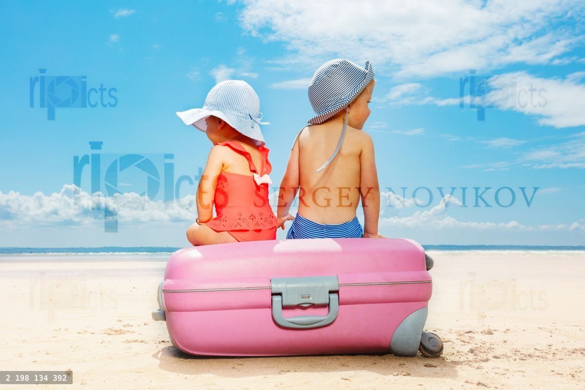 Two children sit on suitcase at the beach concept