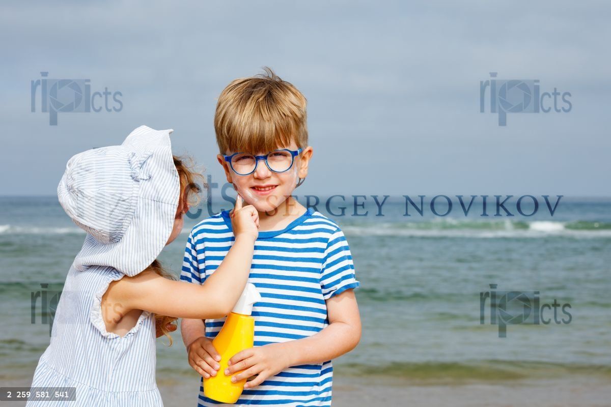 Young girl helps boy with sunscreen at beach in caring gesture