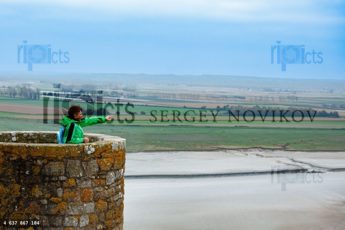 Young boy in green gear enjoying the view from a stone wall