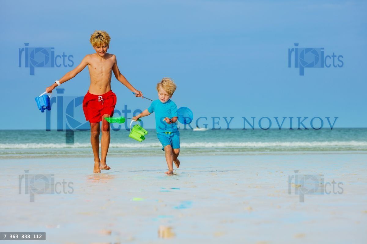 Boys run on a beach hold buckets and hoop net catching crabs