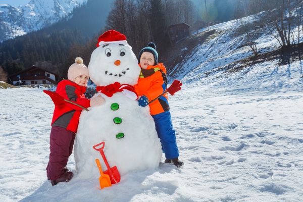 Children in mountains hug funny snowman wearing Santa hat