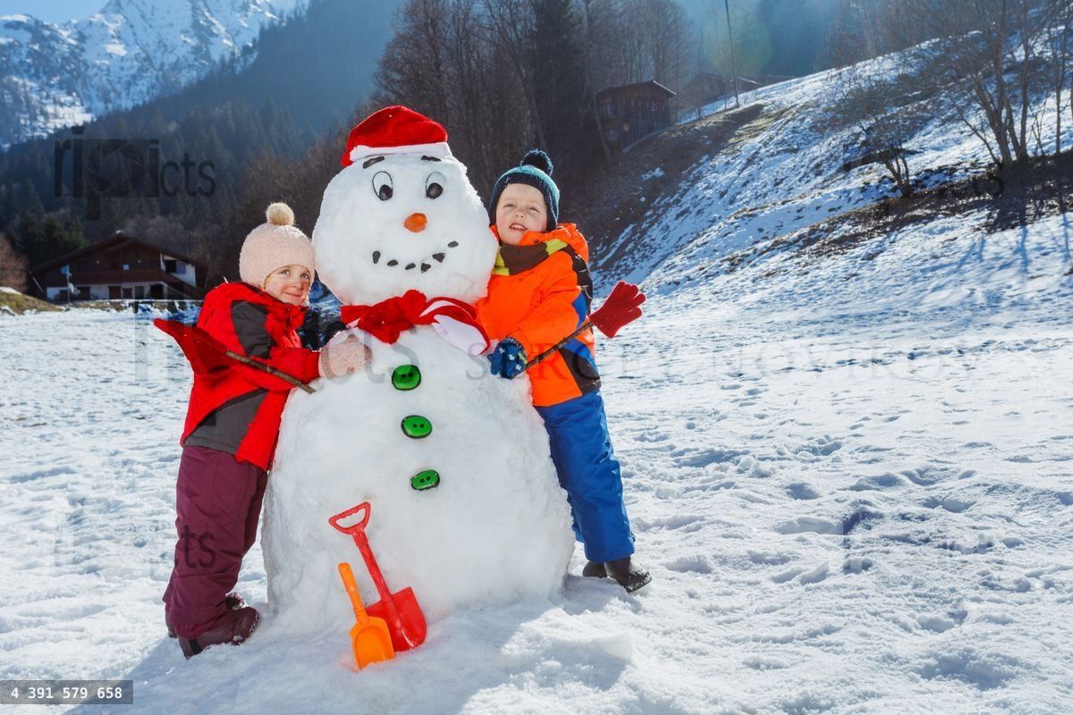 Children in mountains hug funny snowman wearing Santa hat