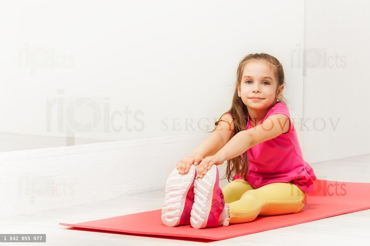 Young gymnast sitting on mat and stretching legs