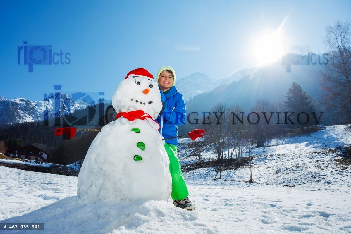 Young boy in winter outfit stand with freshly build snowman