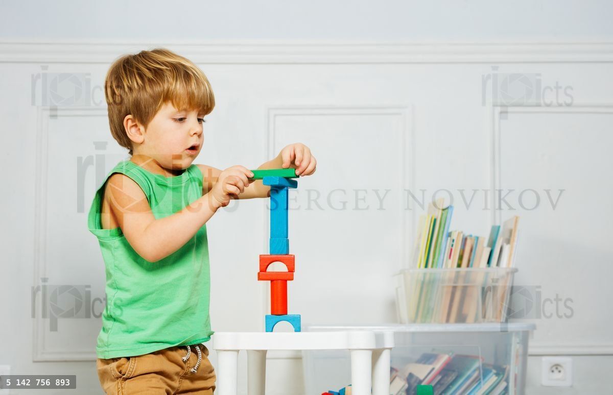 Young boy building block tower amidst books and toys