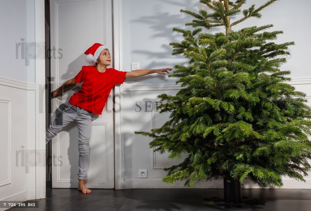 Barefoot child reaches up to decorate the tall Christmas tree