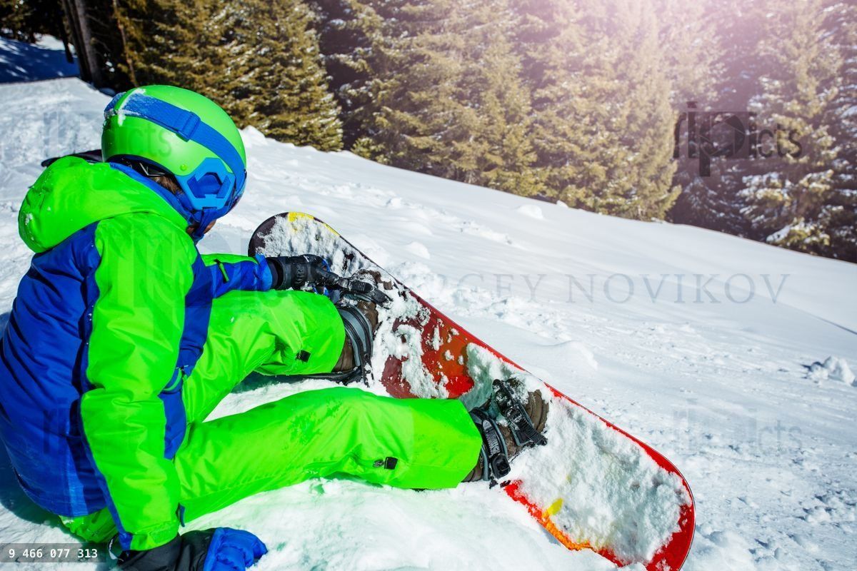 Young boy attaching snowboard sitting in the snow