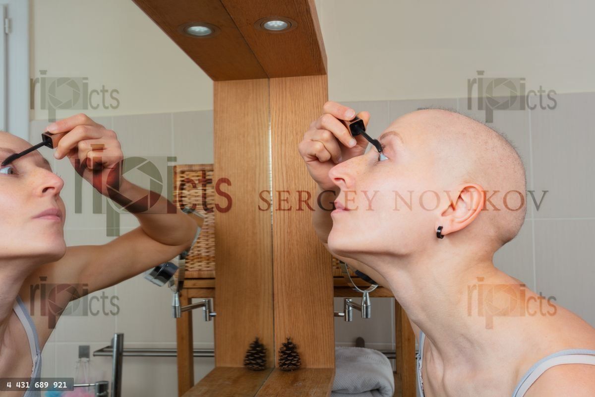 Woman with chemotherapy side effect apply mascara in mirror
