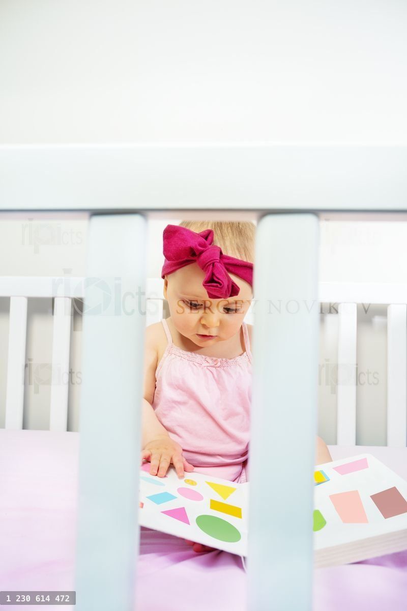 Girl baby sit in crib bed look at book with shapes