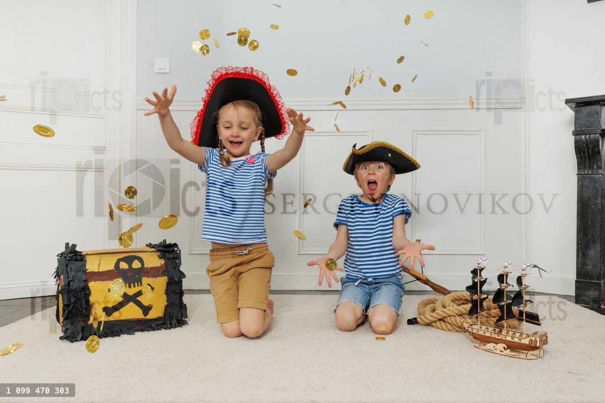Two children toss gold coins over pirate treasure chest by ship