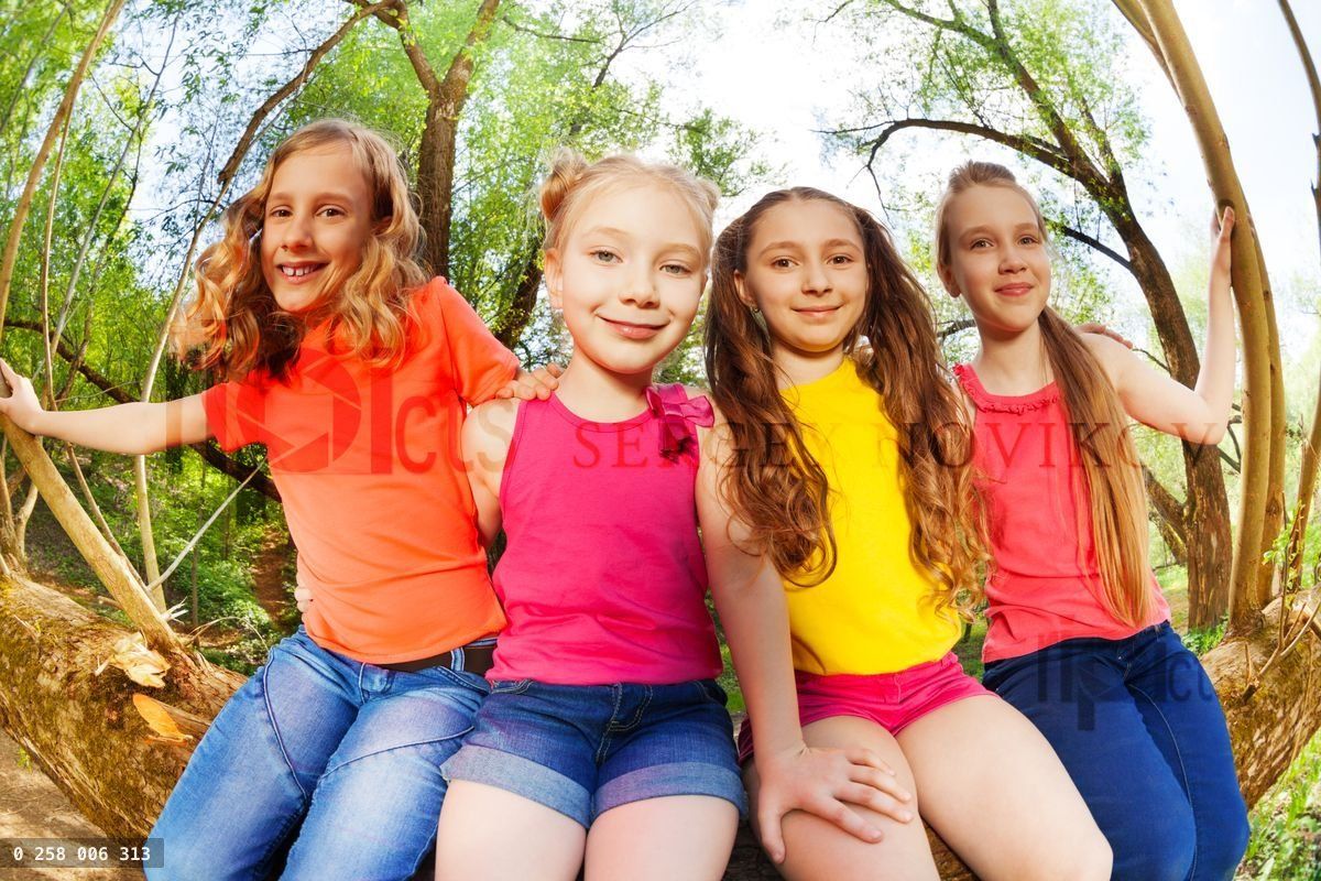 Four happy girl friends sitting on fallen tree