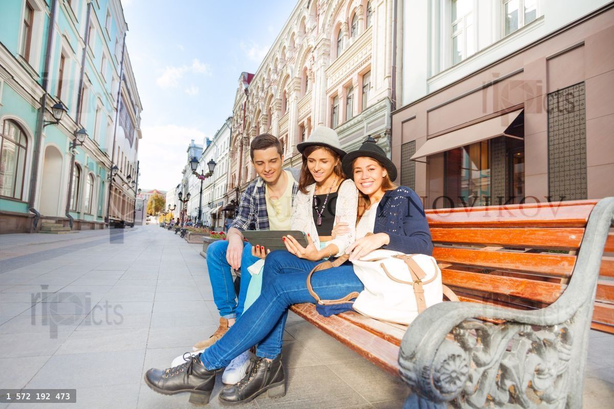 Friends sitting on bench together holding tablet