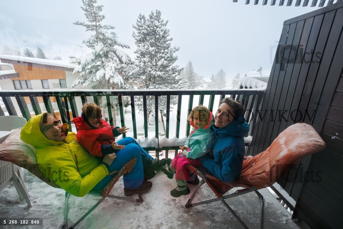 Parents et enfants se détendent sur des chaises pliantes sur le balcon enneigé de la cabine