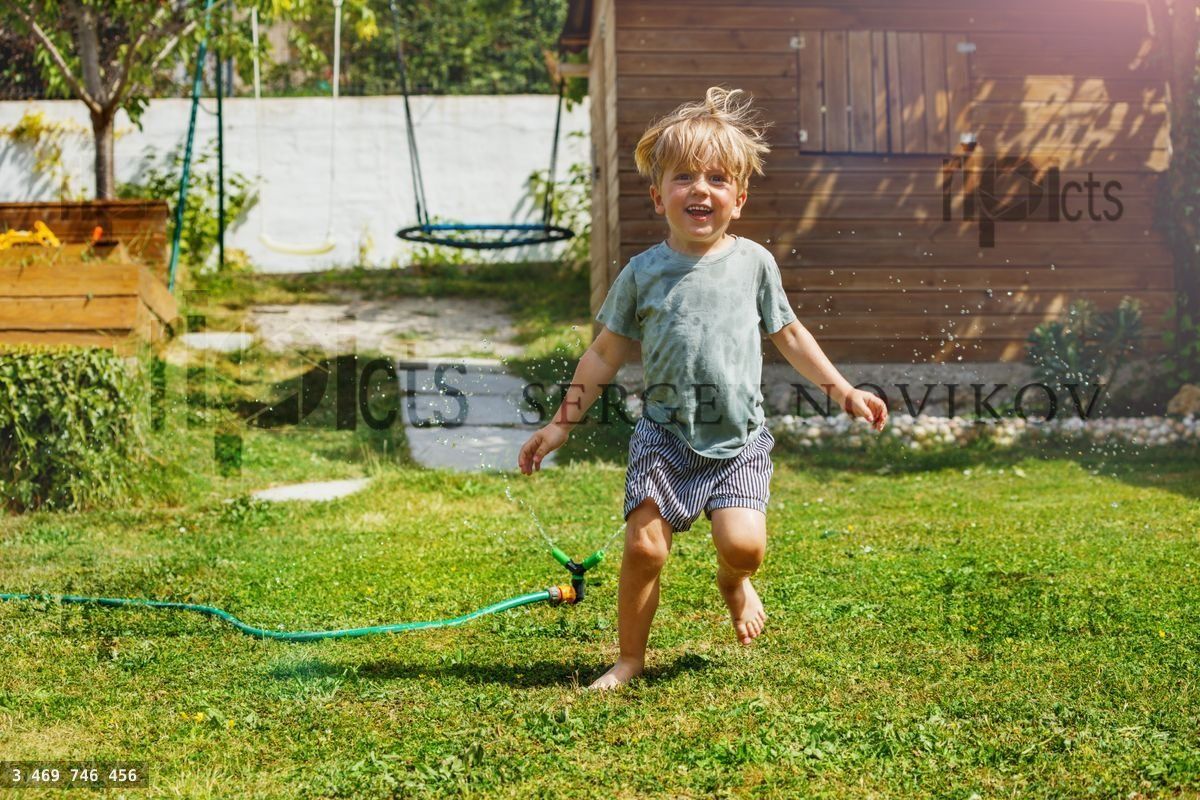 Fun in the garden handsome boy run around water sprinkler