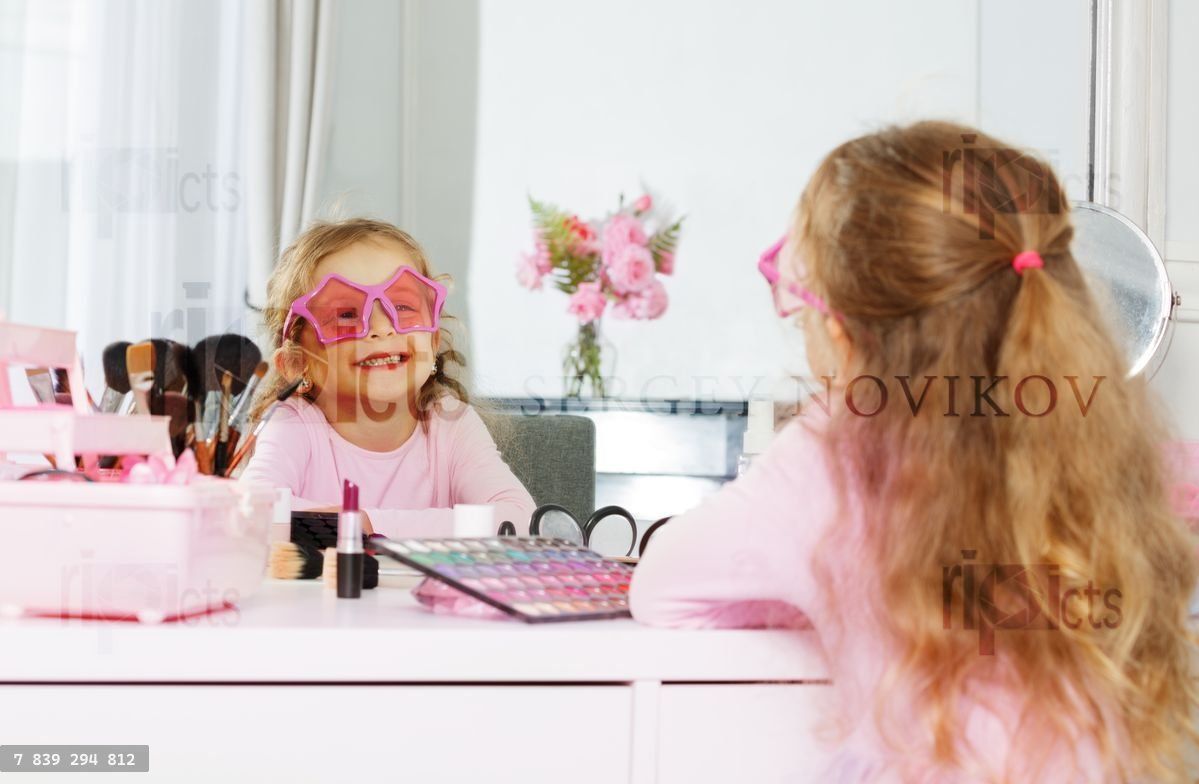 Young girl has fun with makeup and star glasses at vanity table