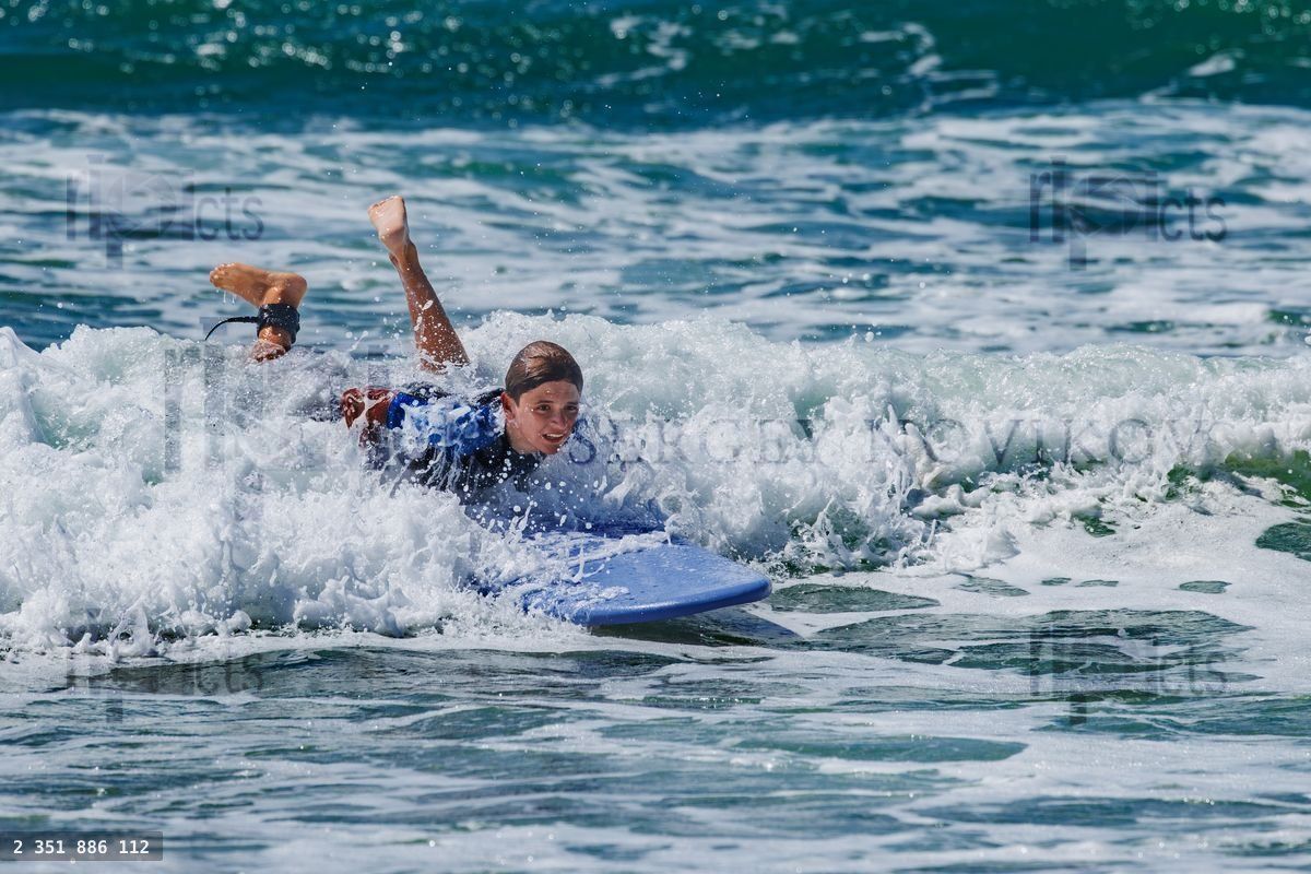 Young teenage surfer at surf school riding a wave on belly