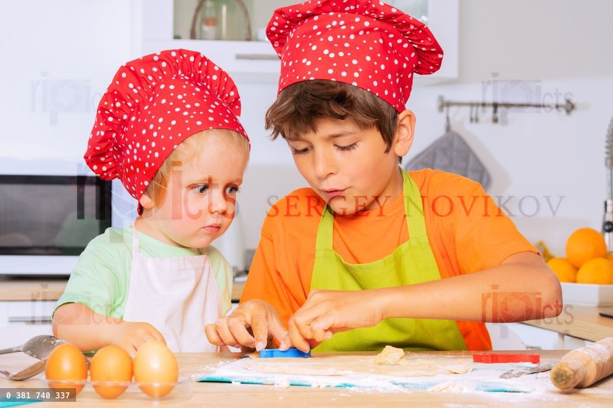 Deux enfants découpent des biscuits en forme de cœur dans de la pâte