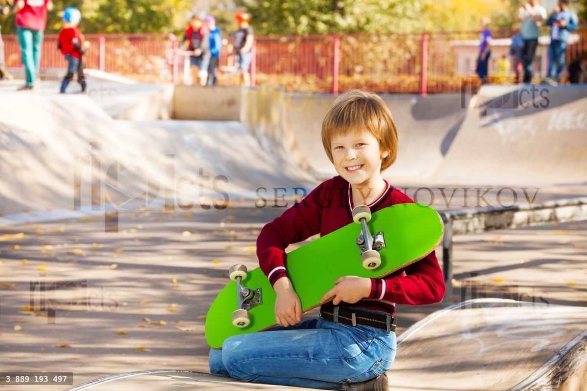 Happy blond boy with green skateboard sitting