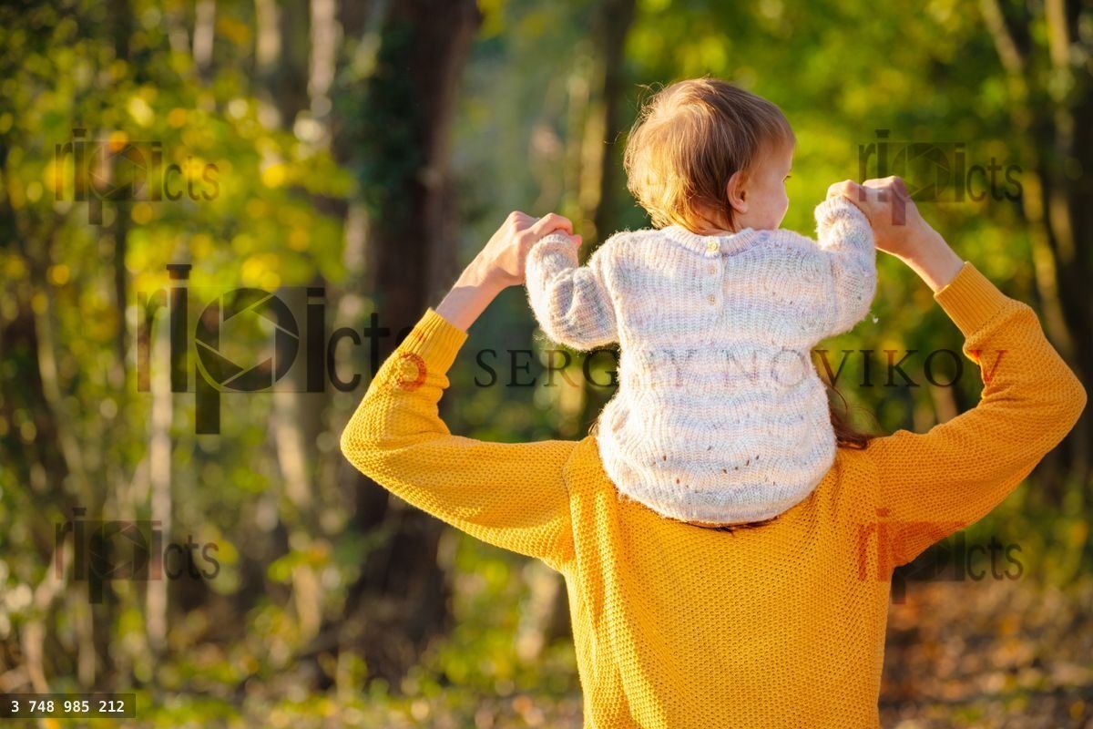 Woman hold her daughter on shoulders in forest