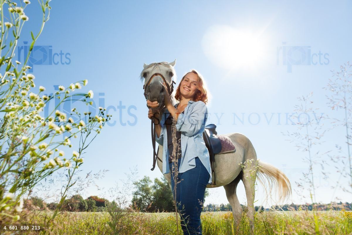 Young woman standing in field with her white horse