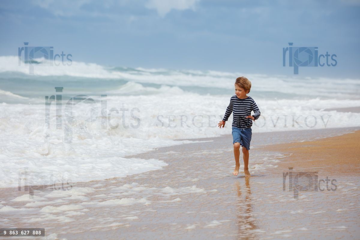 Young boy joyfully runs along a sandy beach's edge on summer day