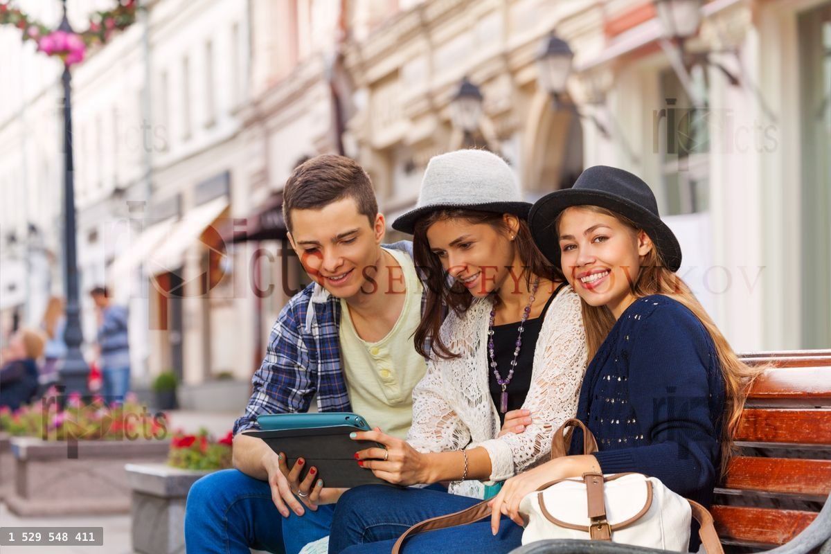 Three friends sit together with tablet on bench