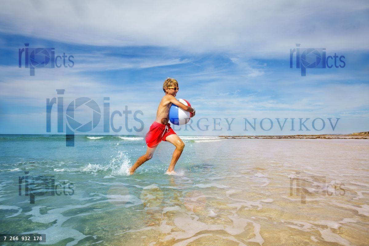 Fun at the beach happy boy run with inflatable ball in waves