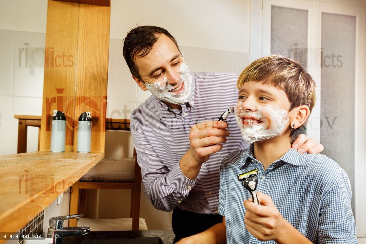 Dad shows son how to shave with razor at bathroom