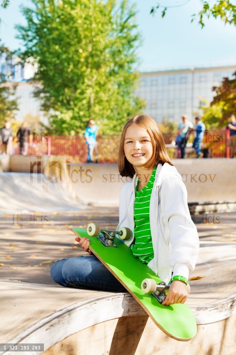 Smiling girl with skateboard sitting on playground