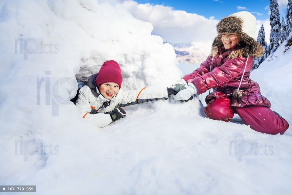 Funny girl pull on her friend from the snow igloo
