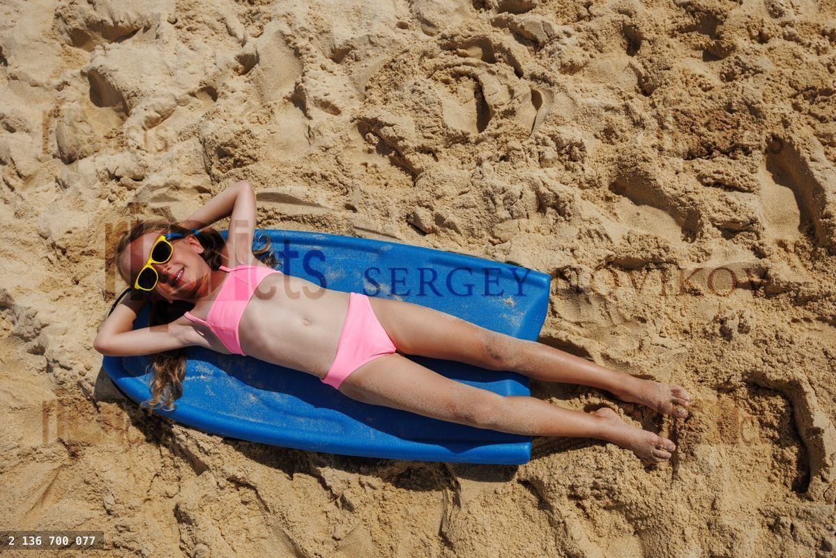 Young girl daydream relaxing on blue surfboard at sandy beach