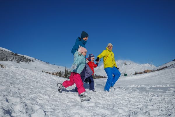 Family strolls together down a snowy hillside under blue sky